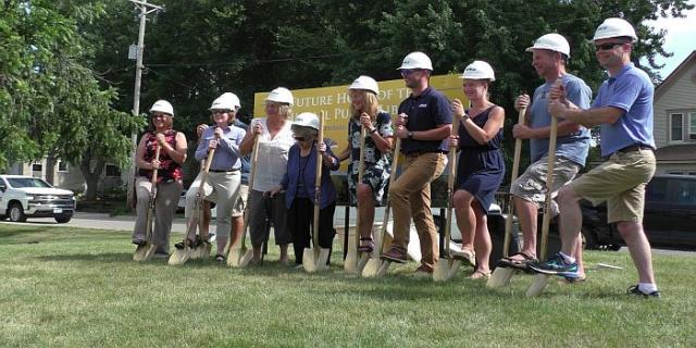 Men and women in hardhats standing next to each other with shovels