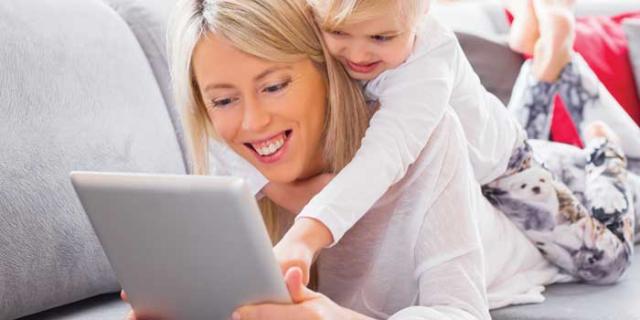 Woman smiling at a tablet with a baby on her back